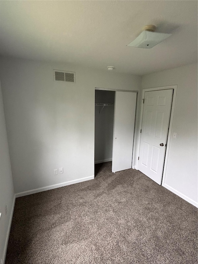 unfurnished bedroom with visible vents, baseboards, dark carpet, and a closet