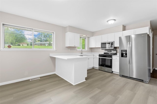 kitchen featuring visible vents, a peninsula, light countertops, light wood finished floors, and stainless steel appliances