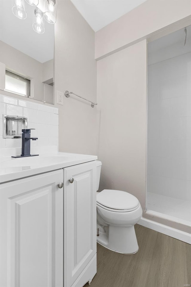 full bathroom with vanity, toilet, decorative backsplash, wood finished floors, and tiled shower