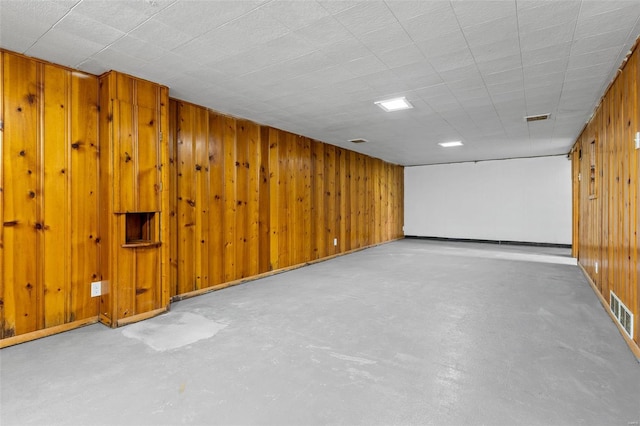 finished below grade area with baseboards, wood walls, and visible vents