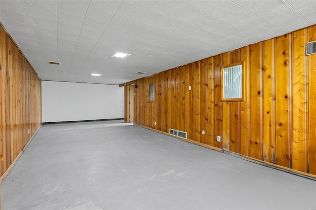 below grade area featuring wood walls, visible vents, and baseboards