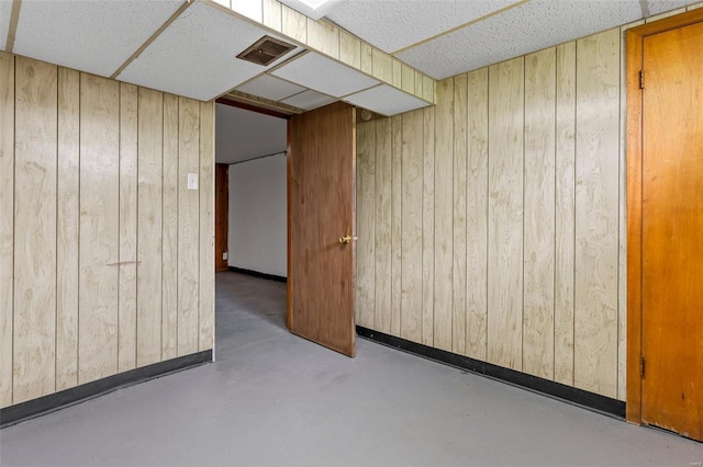 spare room featuring baseboards, concrete flooring, wood walls, and visible vents