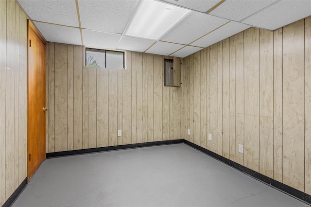 basement featuring baseboards, wood walls, and a drop ceiling