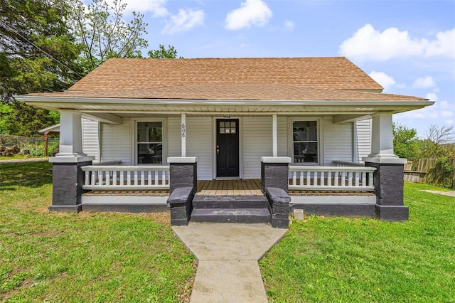 bungalow-style house featuring roof with shingles, covered porch, and a front lawn