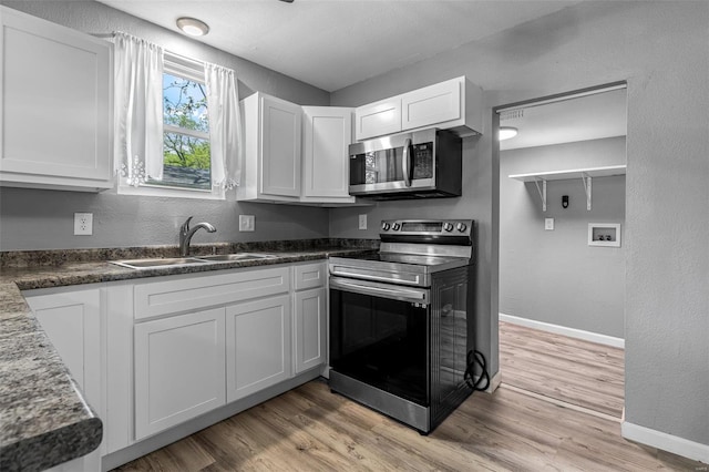 kitchen with white cabinets, appliances with stainless steel finishes, a sink, and light wood-style floors