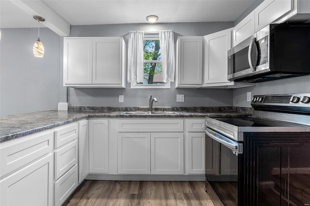 kitchen featuring appliances with stainless steel finishes, a sink, white cabinetry, wood finished floors, and pendant lighting