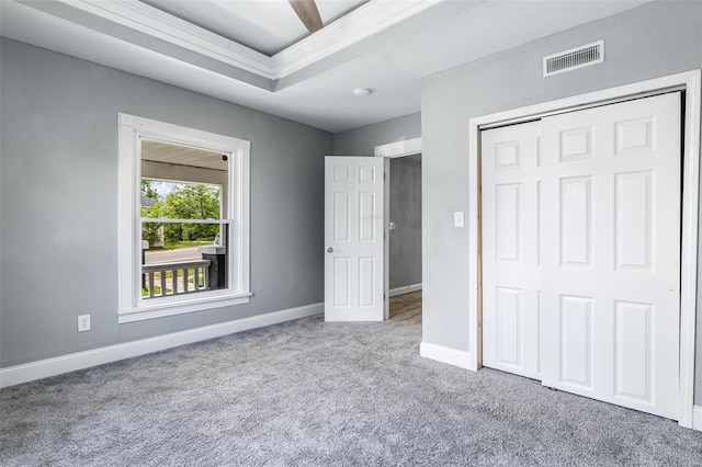 unfurnished bedroom featuring visible vents, baseboards, a closet, carpet, and a tray ceiling