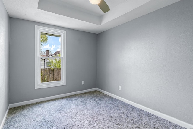 carpeted spare room featuring a ceiling fan, baseboards, and a tray ceiling