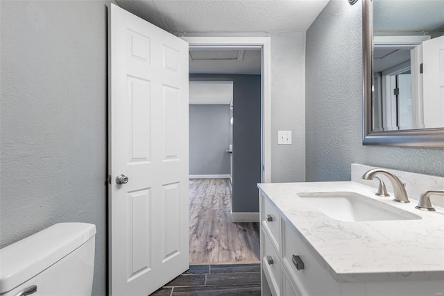 half bathroom featuring vanity, a textured wall, wood finished floors, toilet, and baseboards