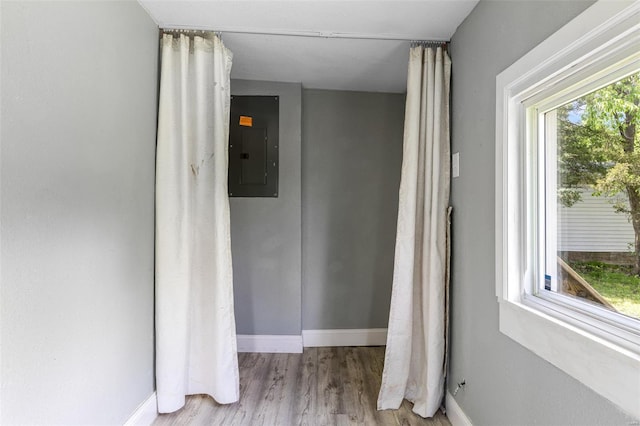 hallway with baseboards, wood finished floors, and electric panel