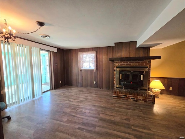 unfurnished living room with visible vents, wood walls, a wood stove, wood finished floors, and a notable chandelier