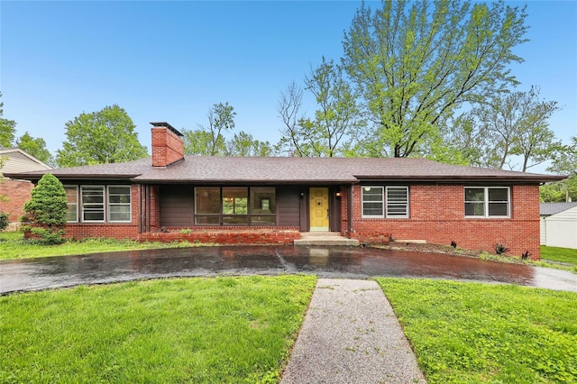 single story home with a chimney, a front yard, and brick siding
