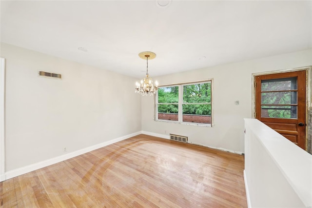 empty room featuring baseboards, light wood-style floors, a chandelier, and visible vents