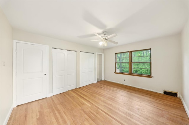 unfurnished bedroom featuring light wood-style flooring, multiple closets, visible vents, baseboards, and ceiling fan