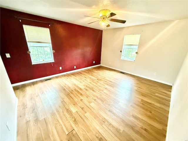 unfurnished room featuring plenty of natural light, ceiling fan, wood finished floors, and visible vents