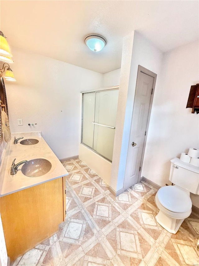 bathroom featuring toilet, baseboards, a sink, and shower / bath combination with glass door