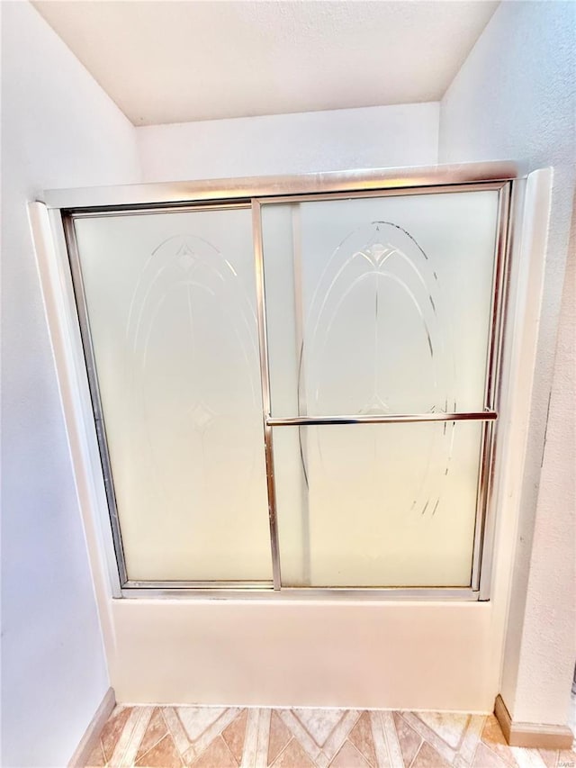 bathroom featuring bath / shower combo with glass door and baseboards
