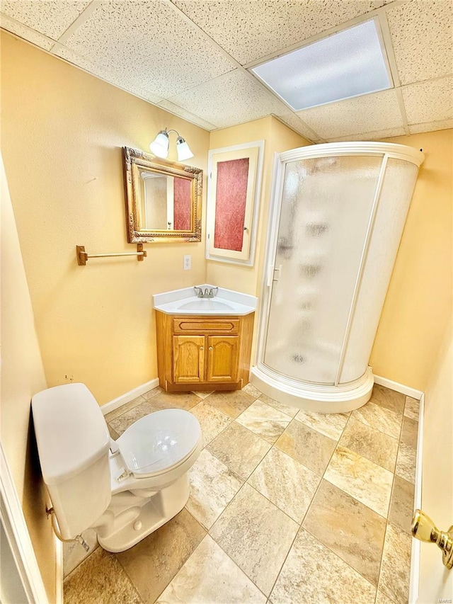 bathroom with vanity, toilet, baseboards, a drop ceiling, and a shower stall