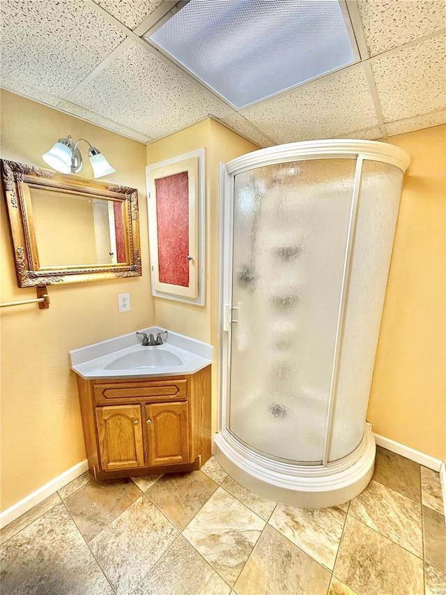 bathroom featuring baseboards, a stall shower, a drop ceiling, and vanity