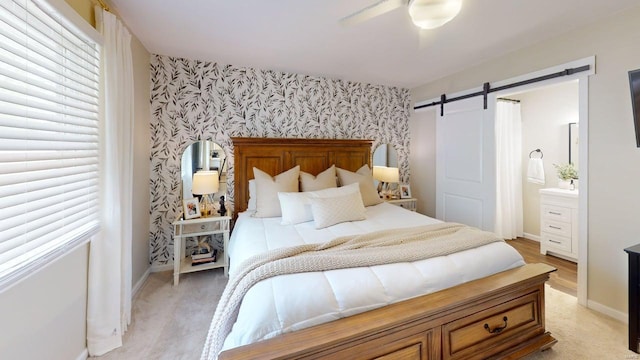 bedroom with connected bathroom, a barn door, an accent wall, wallpapered walls, and baseboards