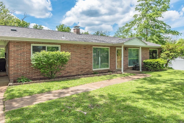ranch-style house with roof with shingles, a front lawn, a chimney, and brick siding