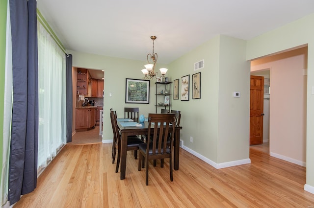 dining room featuring baseboards, an inviting chandelier, visible vents, and light wood-style flooring