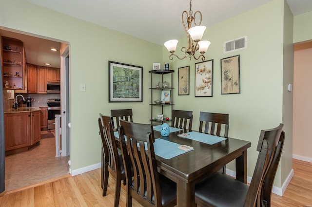 dining room featuring light wood finished floors, visible vents, baseboards, and a notable chandelier