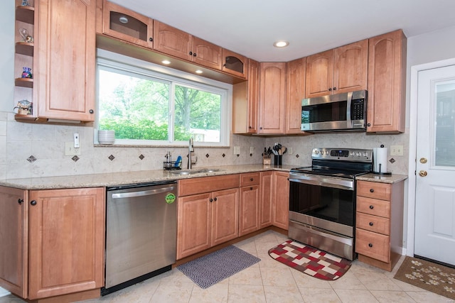 kitchen featuring light stone countertops, tasteful backsplash, appliances with stainless steel finishes, and a sink