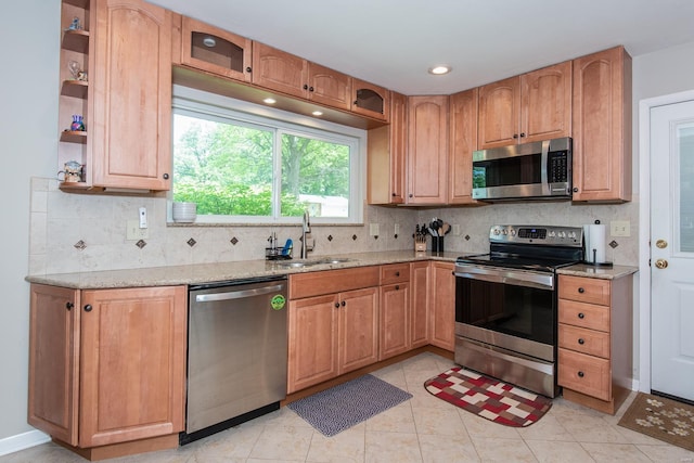 kitchen with appliances with stainless steel finishes, tasteful backsplash, light stone countertops, and a sink