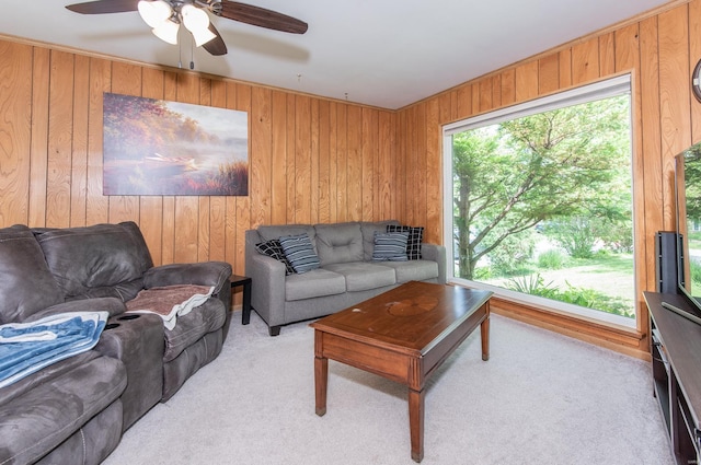 living room with wood walls, ceiling fan, and light colored carpet