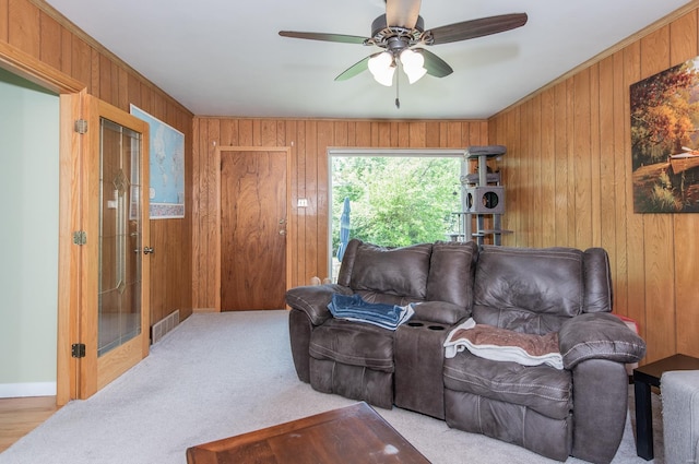 carpeted living area with wood walls, a ceiling fan, and visible vents