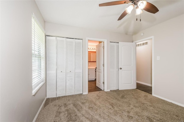 unfurnished bedroom featuring visible vents, multiple closets, baseboards, ensuite bathroom, and carpet flooring