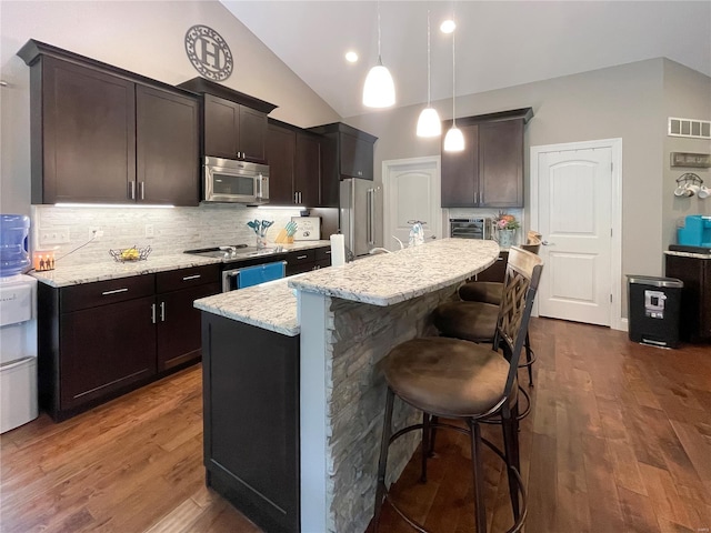 kitchen with decorative backsplash, a kitchen island with sink, light stone counters, a breakfast bar, and stainless steel appliances