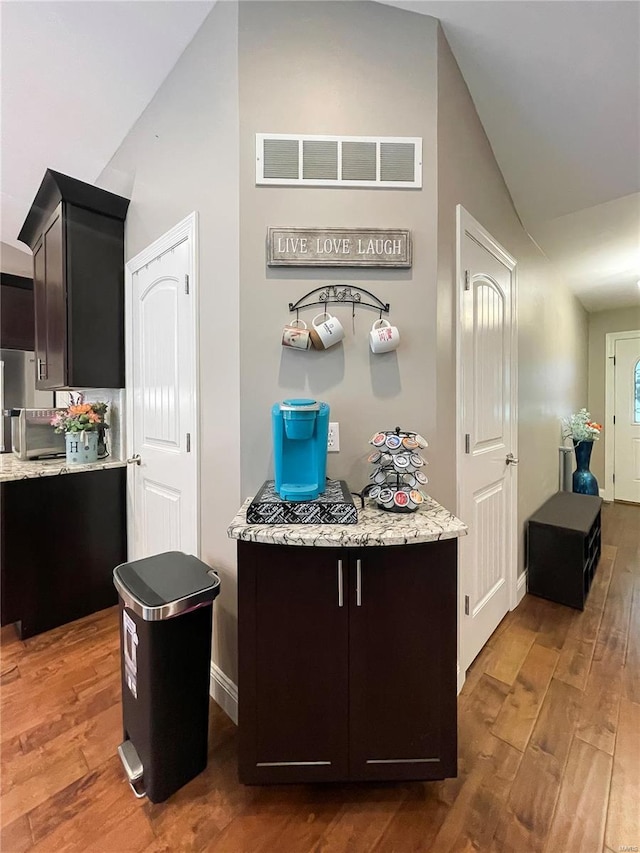 kitchen with visible vents, wood finished floors, lofted ceiling, light stone countertops, and baseboards