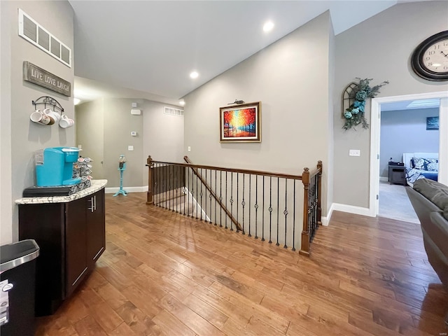 corridor featuring light wood-type flooring, baseboards, vaulted ceiling, and an upstairs landing