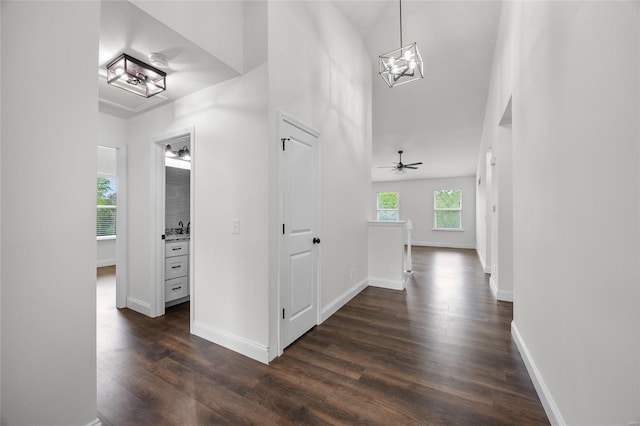 corridor with dark wood-type flooring, baseboards, a towering ceiling, and a chandelier