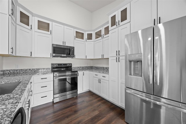 kitchen featuring glass insert cabinets, white cabinets, light stone counters, dark wood finished floors, and appliances with stainless steel finishes