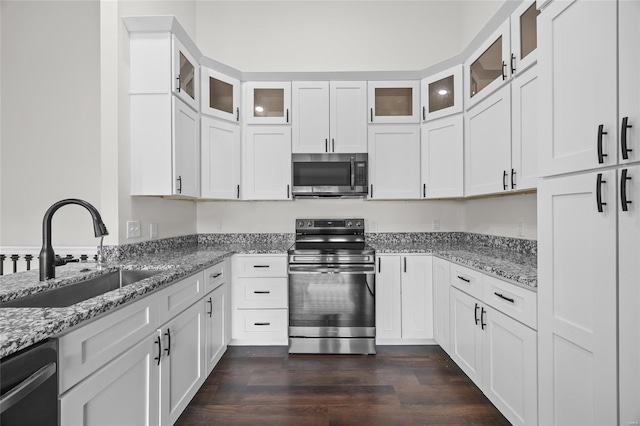 kitchen with light stone countertops, a sink, white cabinets, stainless steel appliances, and dark wood-type flooring