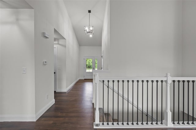 corridor featuring baseboards, dark wood-style flooring, a chandelier, and an upstairs landing