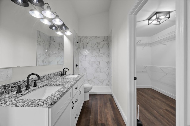 bathroom with double vanity, a walk in closet, wood finished floors, a sink, and a walk in shower