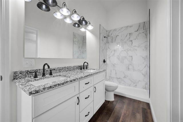 bathroom with double vanity, tiled shower, a sink, and wood finished floors