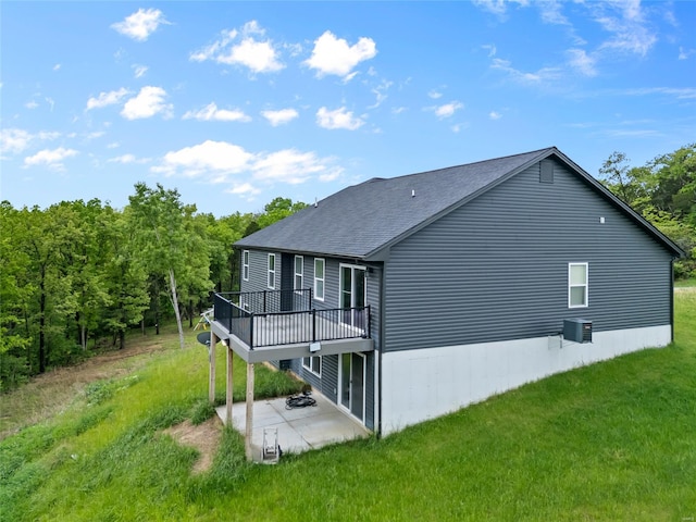 rear view of property featuring a yard, a patio, a wooden deck, and roof with shingles