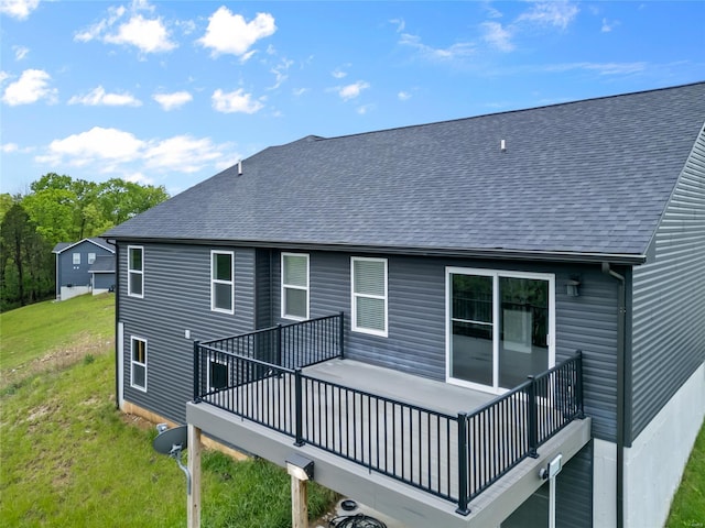 rear view of house featuring a lawn, a wooden deck, and roof with shingles