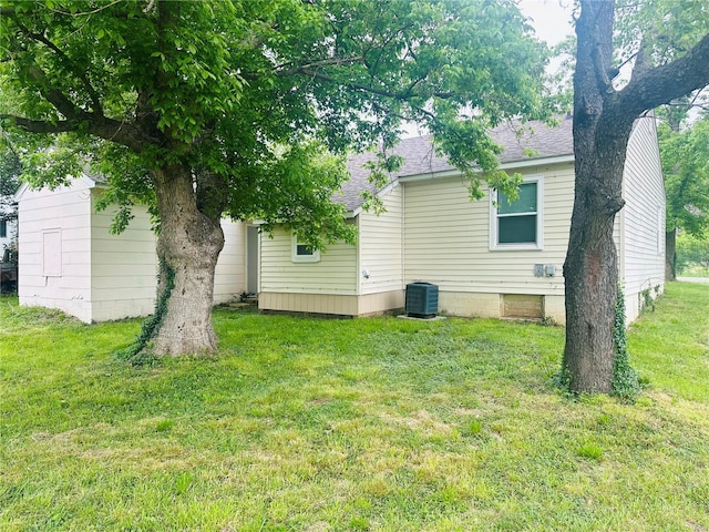 back of property with central air condition unit, a lawn, and roof with shingles