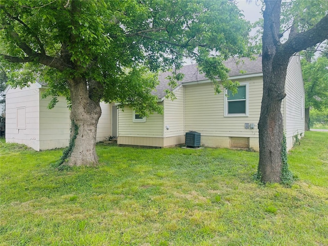 rear view of property featuring a lawn, roof with shingles, and cooling unit