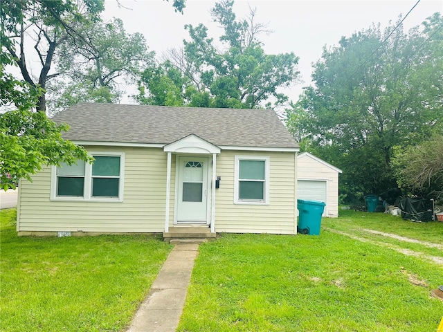 bungalow-style house with a front lawn, roof with shingles, and an outbuilding
