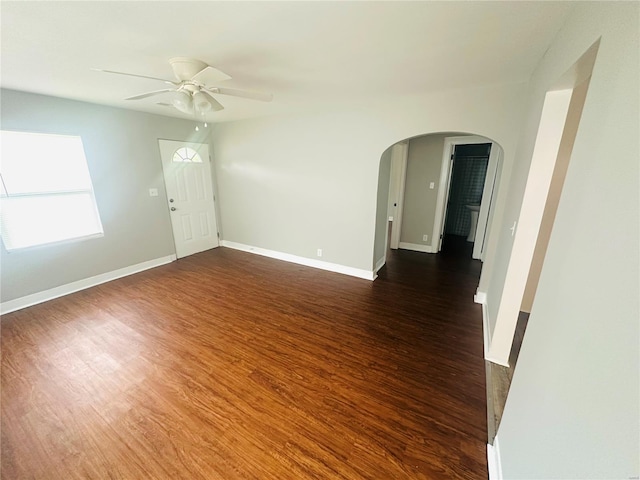 unfurnished room with arched walkways, baseboards, a ceiling fan, and dark wood finished floors