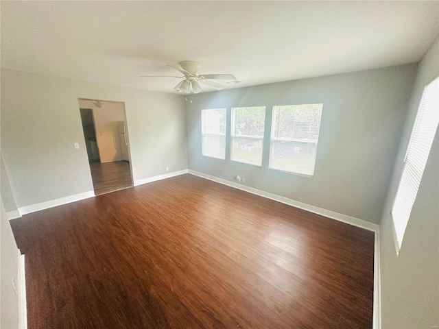 empty room with dark wood-type flooring, a ceiling fan, and baseboards