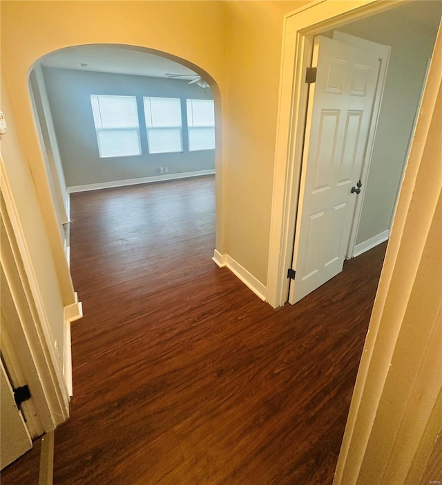 hall with dark wood-type flooring, arched walkways, and baseboards