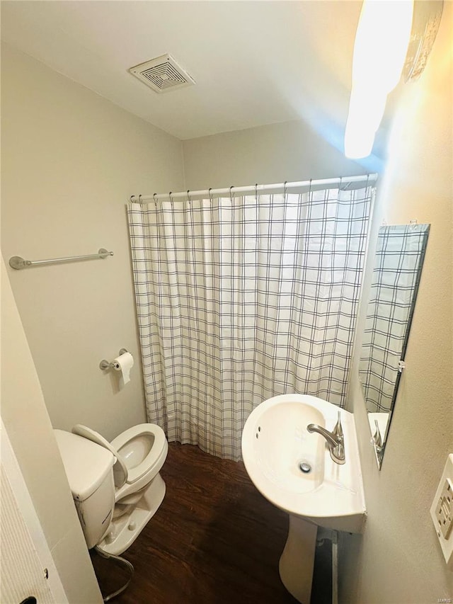 bathroom with a sink, toilet, wood finished floors, a shower with curtain, and visible vents
